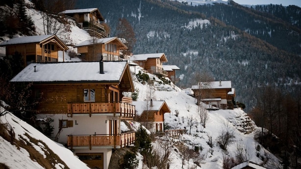 Eine Gruppe Holzhütten mit Balkonen vor einer verschneiten Berglandschaft.