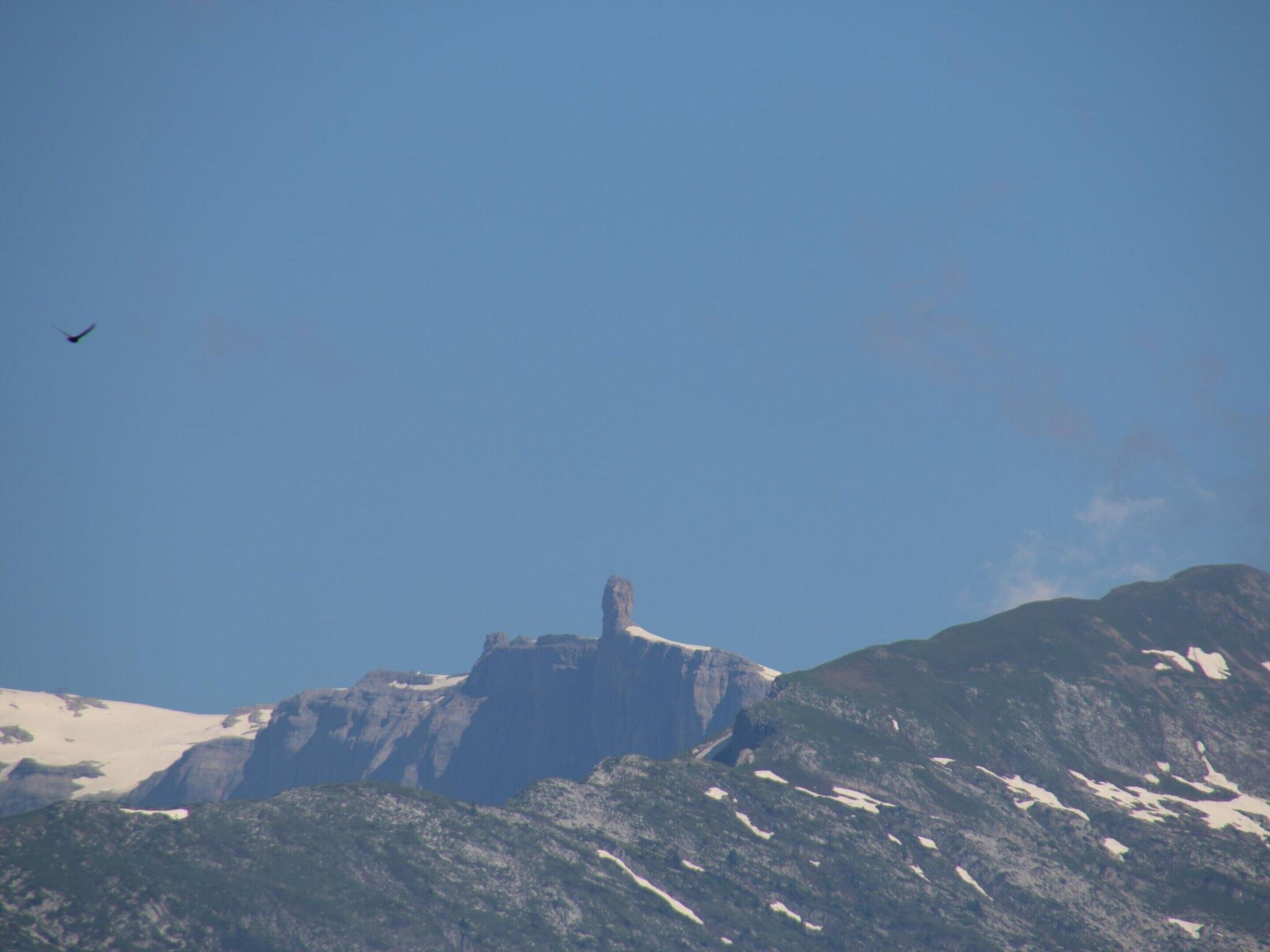 Eine Berglandschaft mit einem markanten Gipfel und einem Vogel im Himmel.