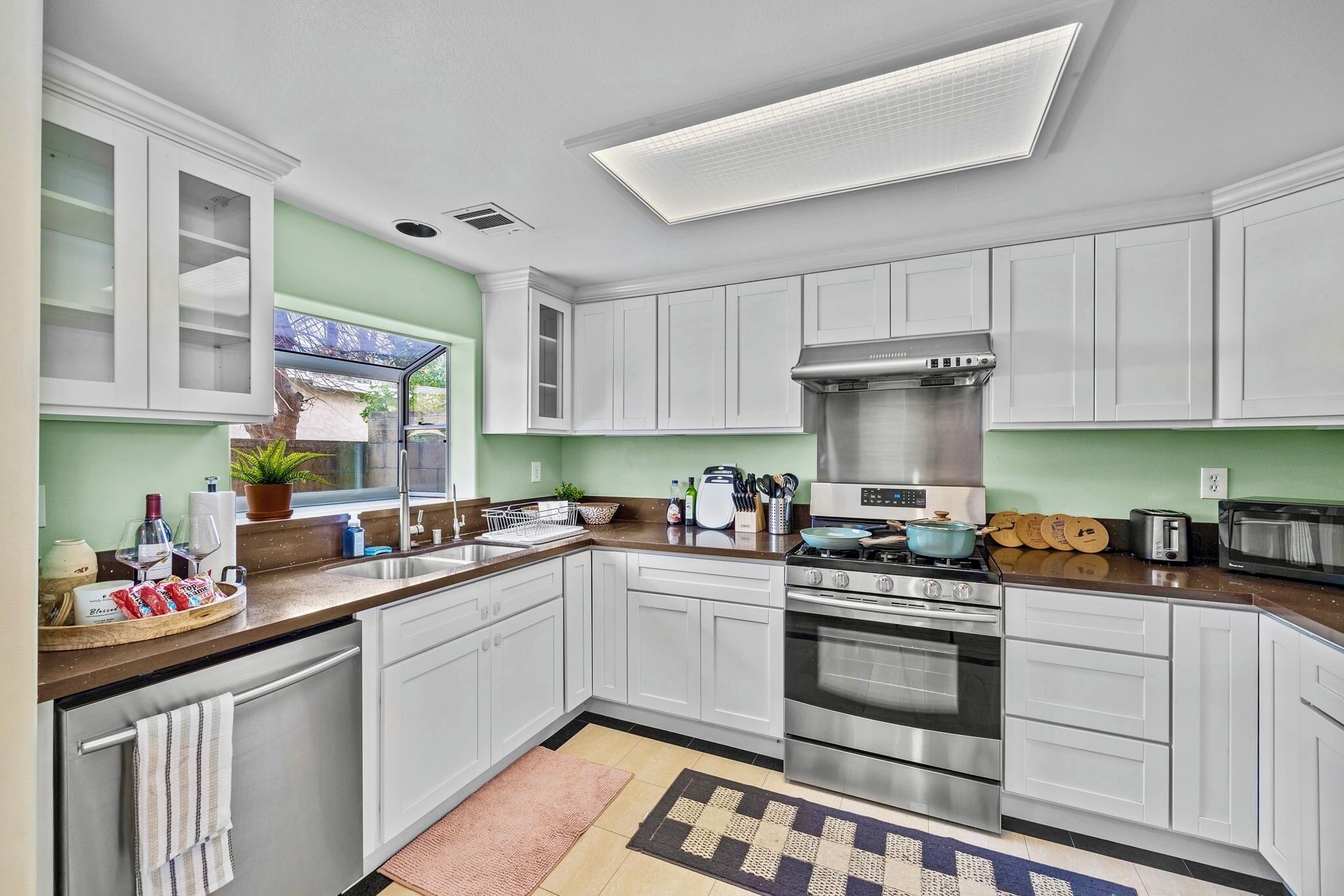 A modern kitchen with white cabinets, stainless steel appliances, and a large window.