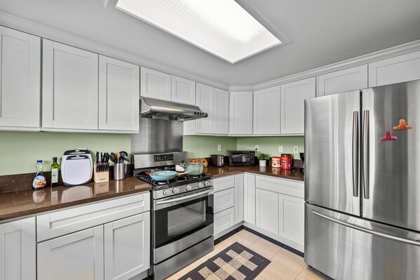 A modern kitchen with white cabinets, stainless steel appliances, and a brown countertop.