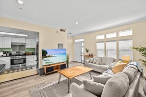 A spacious living area with a large flat-screen TV, a wooden coffee table, and a beige sofa.