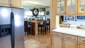 A kitchen with wooden cabinets, a refrigerator, a dining area with chairs, and a bar area with stools. - Stylish Atlanta Retreat! (Atlanta)