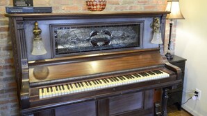 A grand piano with a glass top, positioned against a brick wall. - Stylish Atlanta Retreat! (Atlanta)