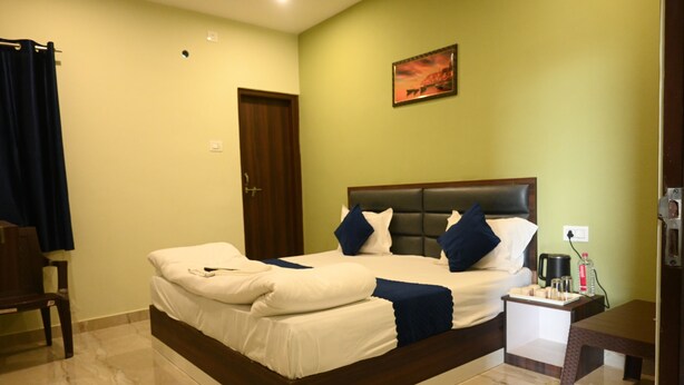 A neatly made bed with white and blue bedding, a bedside table with a lamp, and a painting on the wall. - Hotel Imperial Kashi (Varanasi)