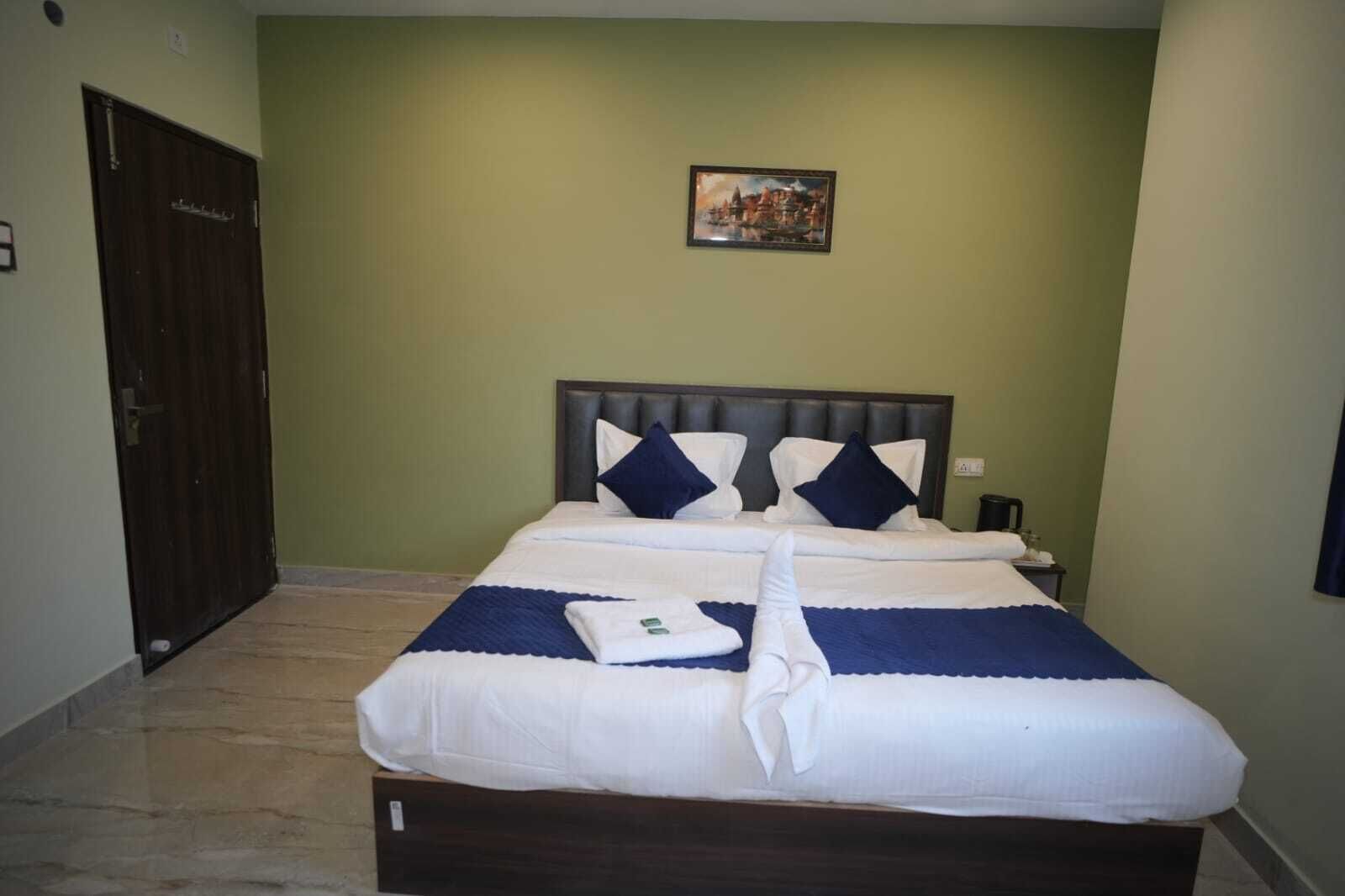 A neatly made double bed with white and blue bedding, a headboard, and a painting on the wall.