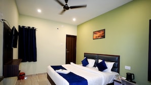 A neatly made bed with a blue and white bedspread, a ceiling fan, a painting on the wall, and a coffee maker on the nightstand. - Hotel Imperial Kashi (Varanasi)