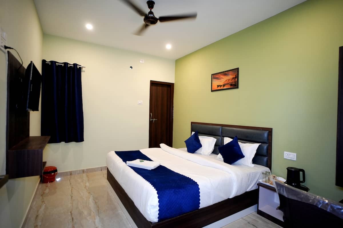 A neatly made bed with a blue and white bedspread, a ceiling fan, a painting on the wall, and a coffee maker on the nightstand.