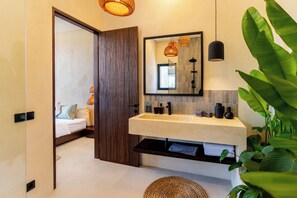 A modern bathroom with a wooden door, a white sink, and a mirror above it. - Villa Balijero by Pertama Stay (Pecatu)