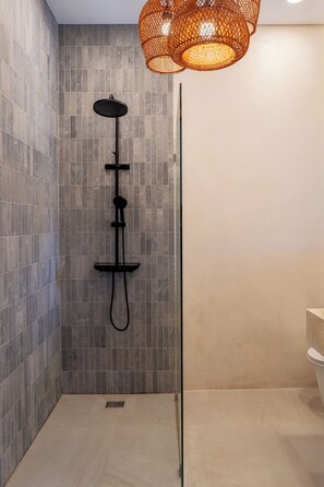 A modern shower with a glass enclosure, a black rain showerhead, and a woven orange light fixture. - Villa Balijero by Pertama Stay (Pecatu)