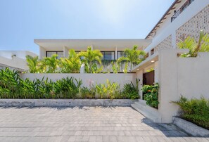 A modern building with a flat roof, large windows, and a paved courtyard with various plants.