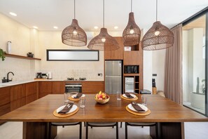 Una cucina moderna con un tavolo da pranzo in legno, lampade a sospensione in vimini e un'ampia finestra.