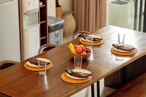 Une table à manger dressée avec des assiettes, des verres et un saladier rempli de fruits.