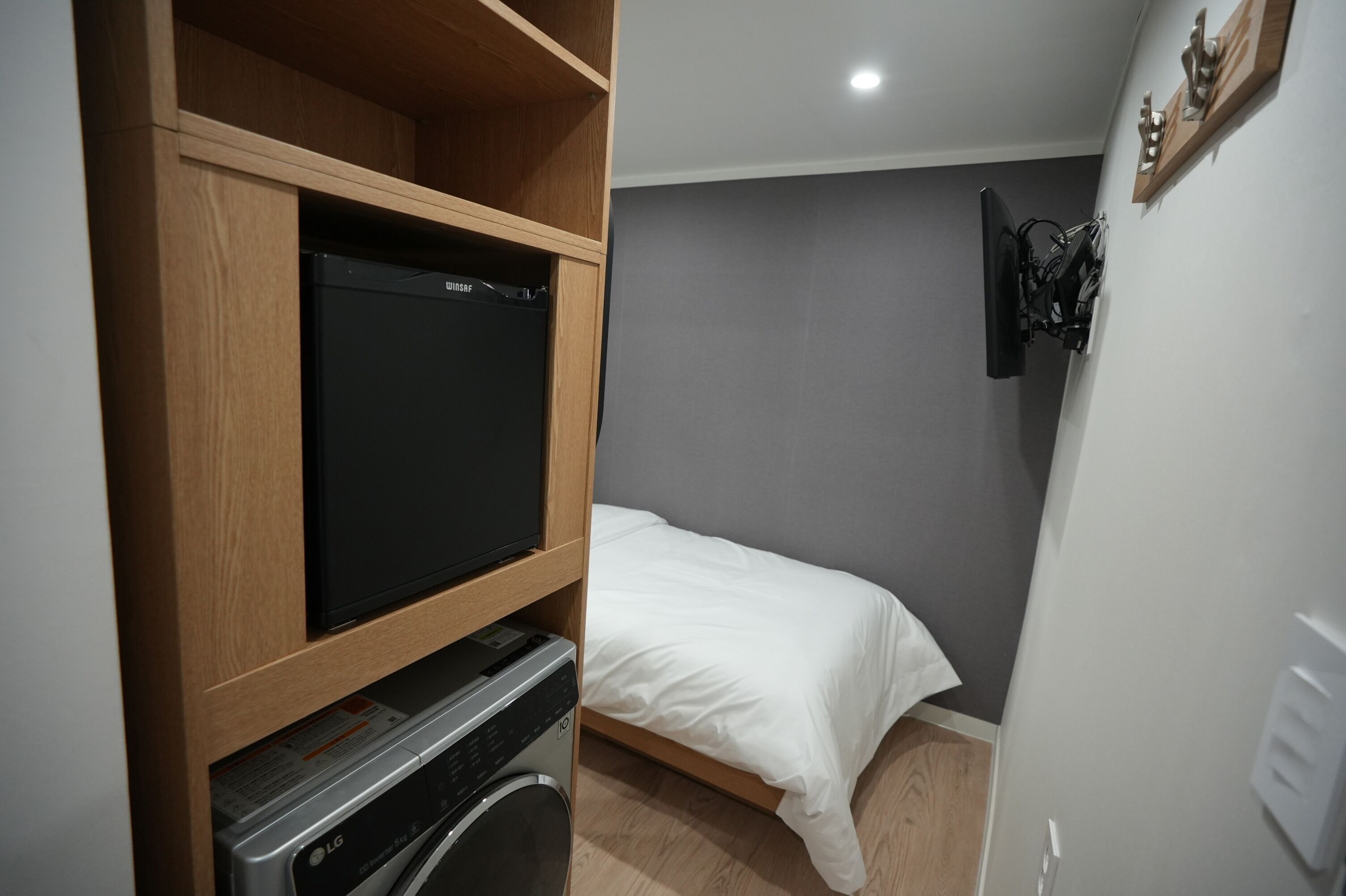 A compact room with a bed, a television on a wooden shelf, and a washing machine.