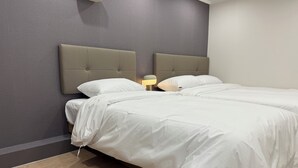 Een tweepersoonsbed met een grijs hoofdeinde en wit beddengoed in een kamer met grijze wanden en houten vloeren.