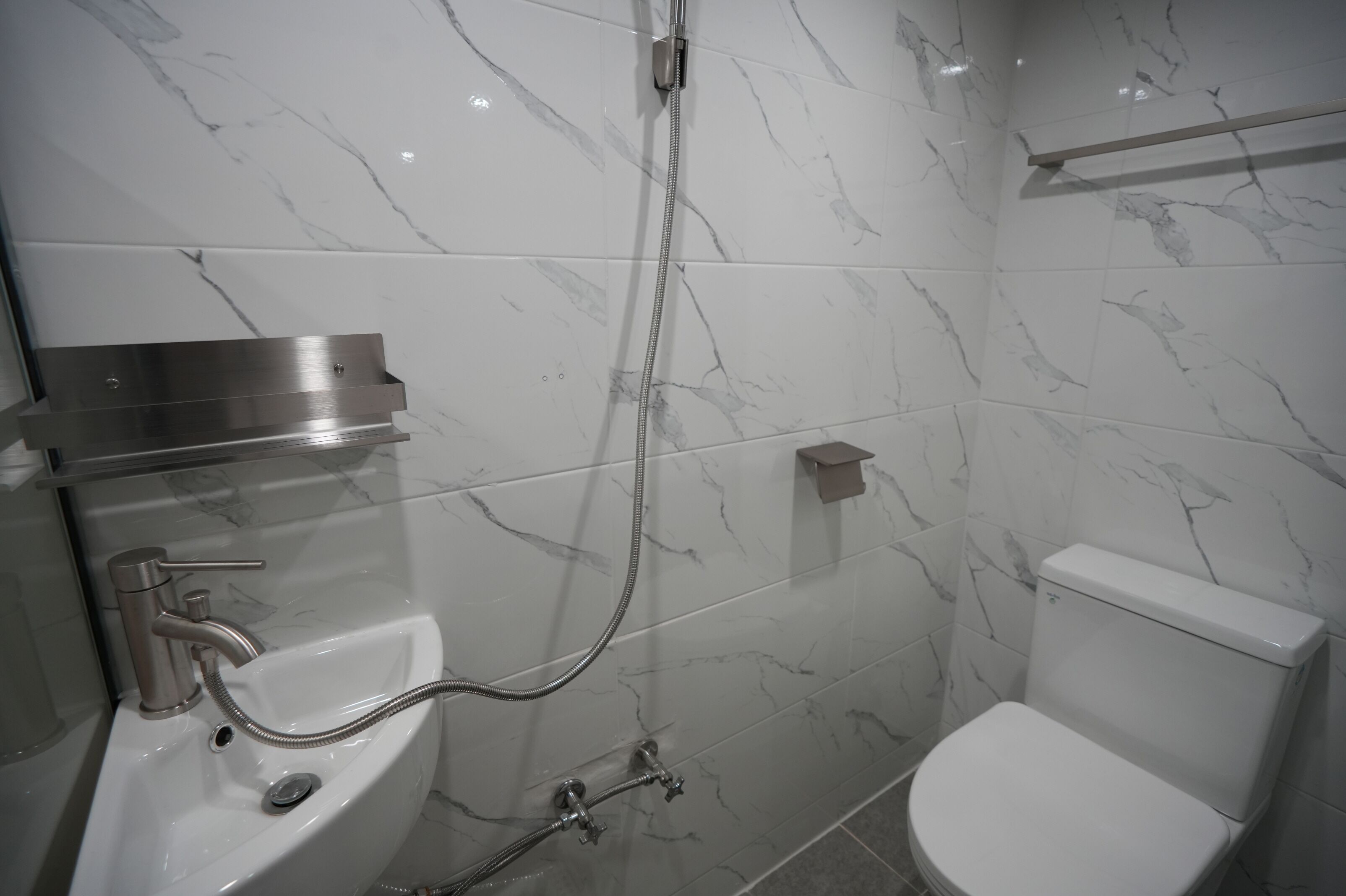 A modern bathroom with a marble backsplash, a sink with a handheld showerhead, and a toilet.