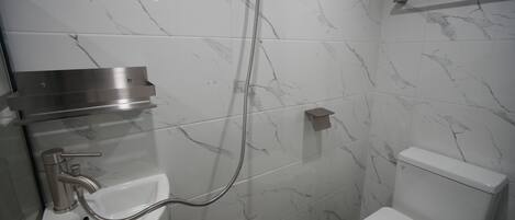 A modern bathroom with a marble backsplash, a sink with a handheld showerhead, and a toilet.