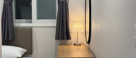 A hotel room with a bed, a bedside table with a lamp, and curtains over a window.
