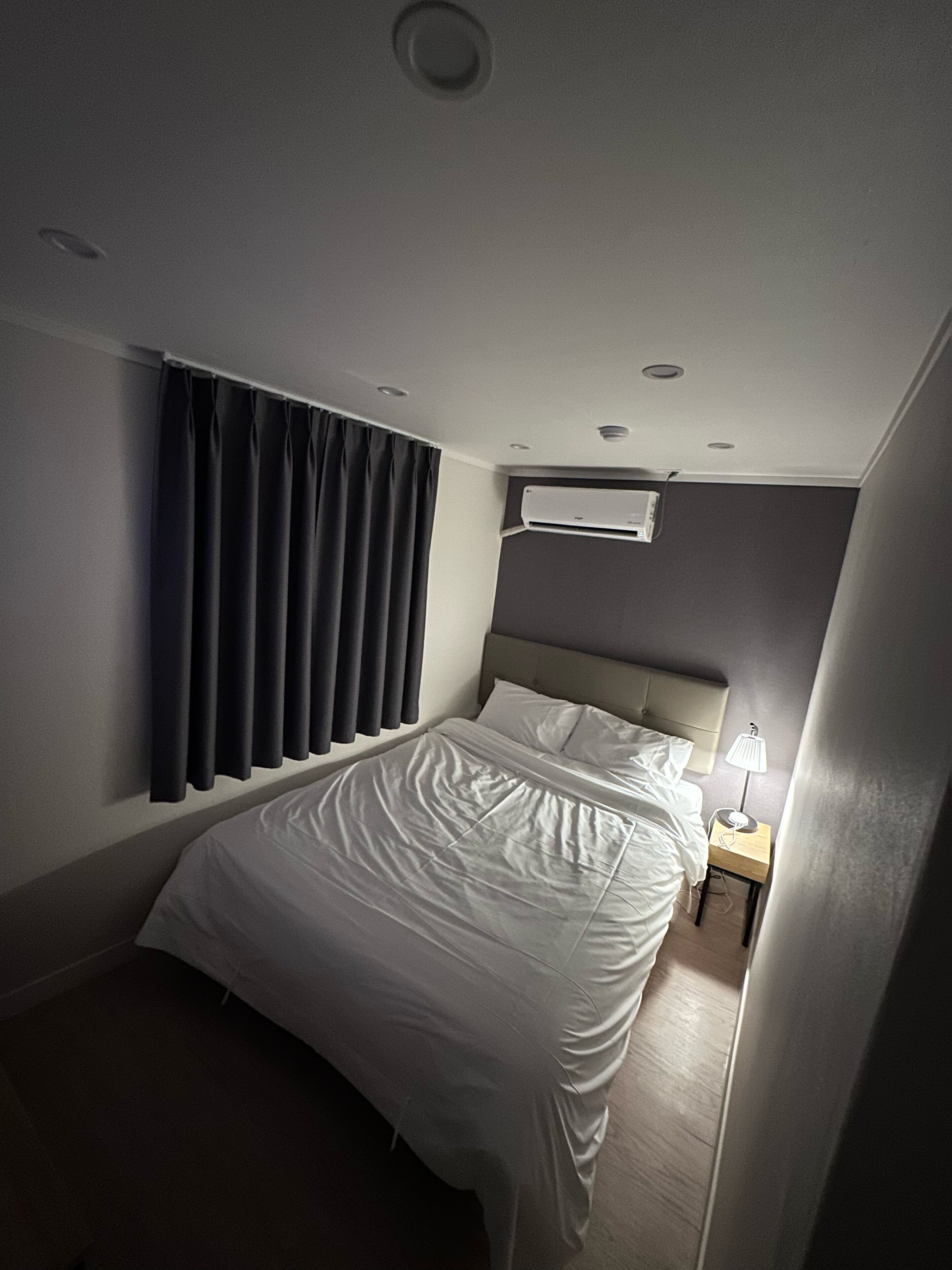 Quarto de hotel com cama, mesa de cabeceira, ar condicionado e janela com cortinas.