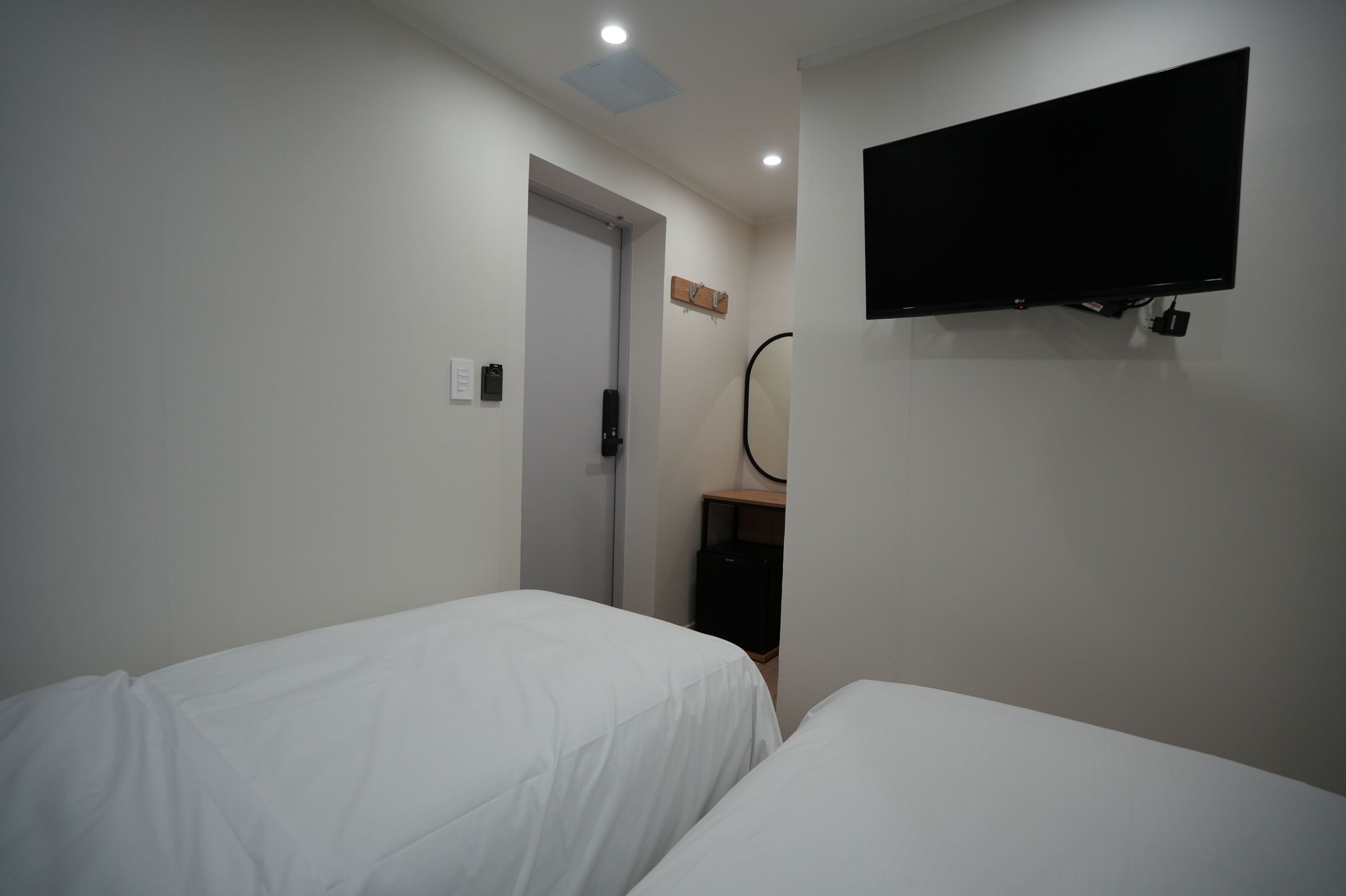 A hotel room with two beds, a television mounted on the wall, a door leading to another room, and a small shelf with a mirror.