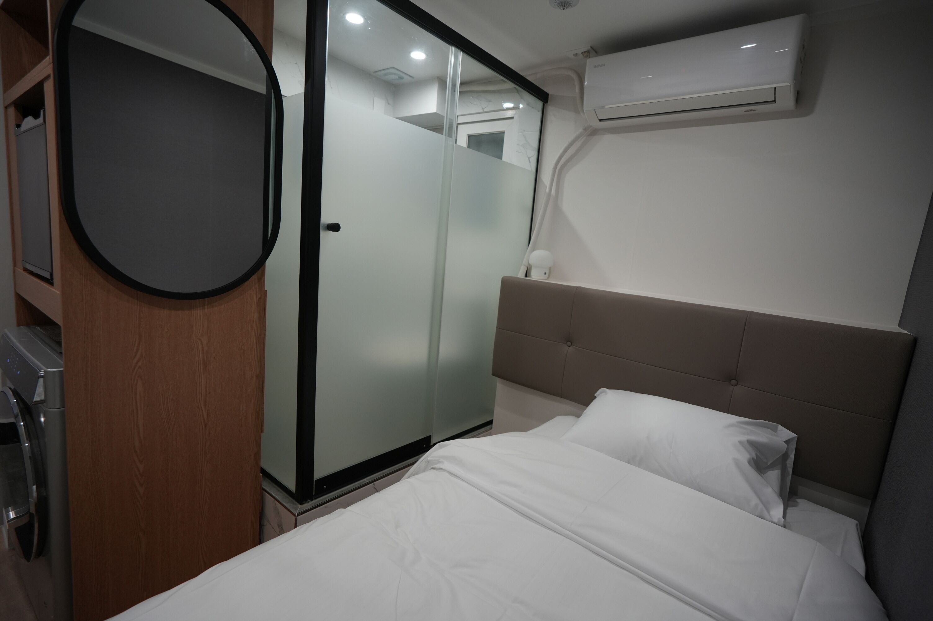 A hotel room with a bed, a wardrobe, a mirror, and an air conditioning unit.
