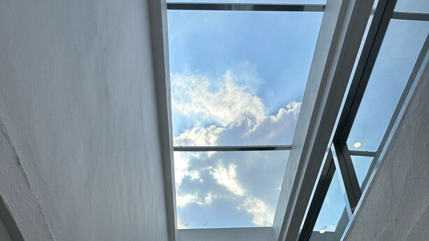 Een dakraam met uitzicht op de lucht en wolken, een klein raam en wandlampen.
