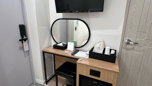 Hotelkamer met een bureau, een aan de muur bevestigde televisie, een spiegel, een prullenbak en een garderobe.