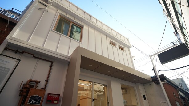 Ein Gebäude mit weißer Fassade, einem sichtbaren Eingang und einer Feuerleiter links.