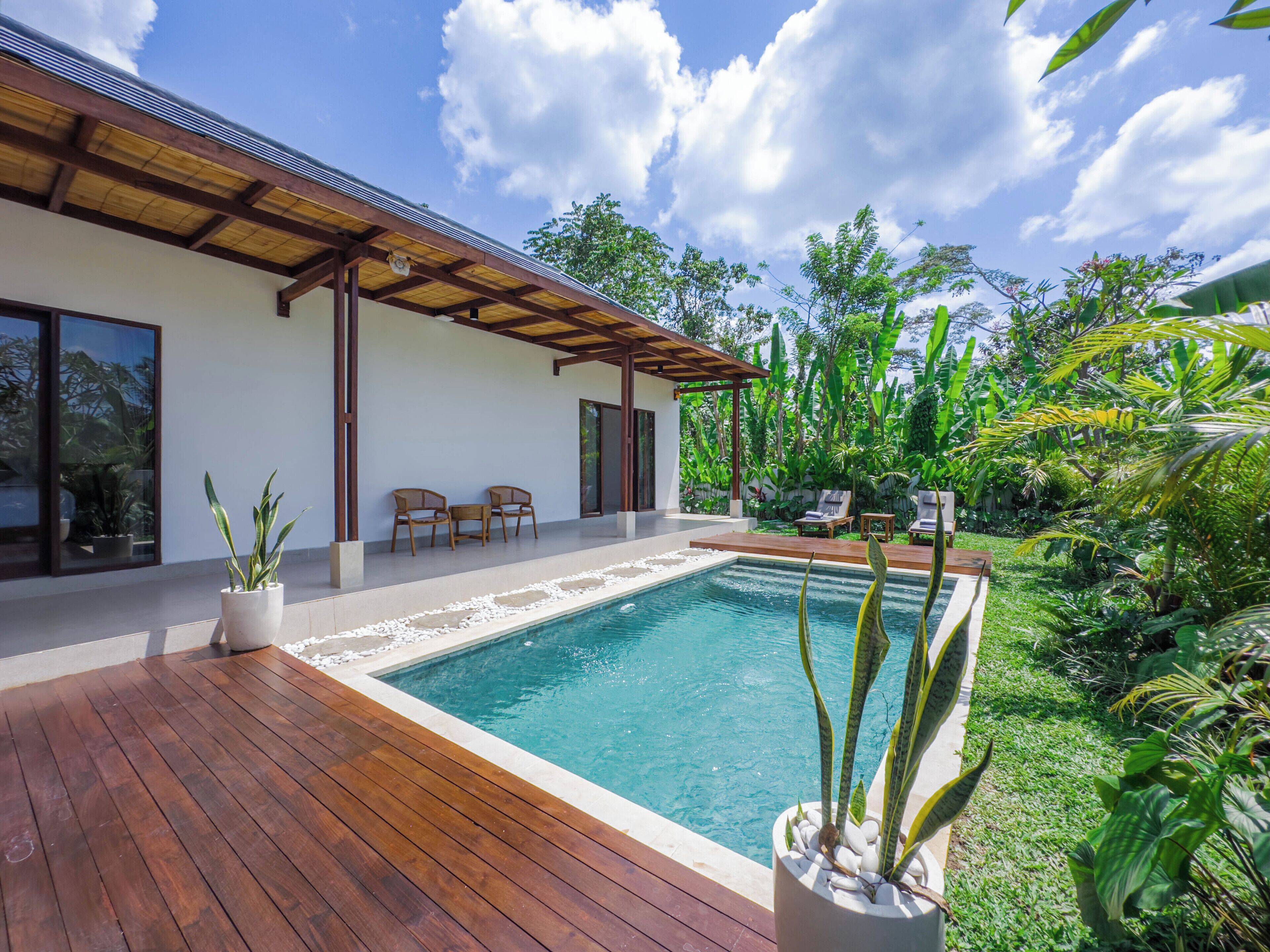 A modern house with a wooden deck, a swimming pool, and lush greenery.