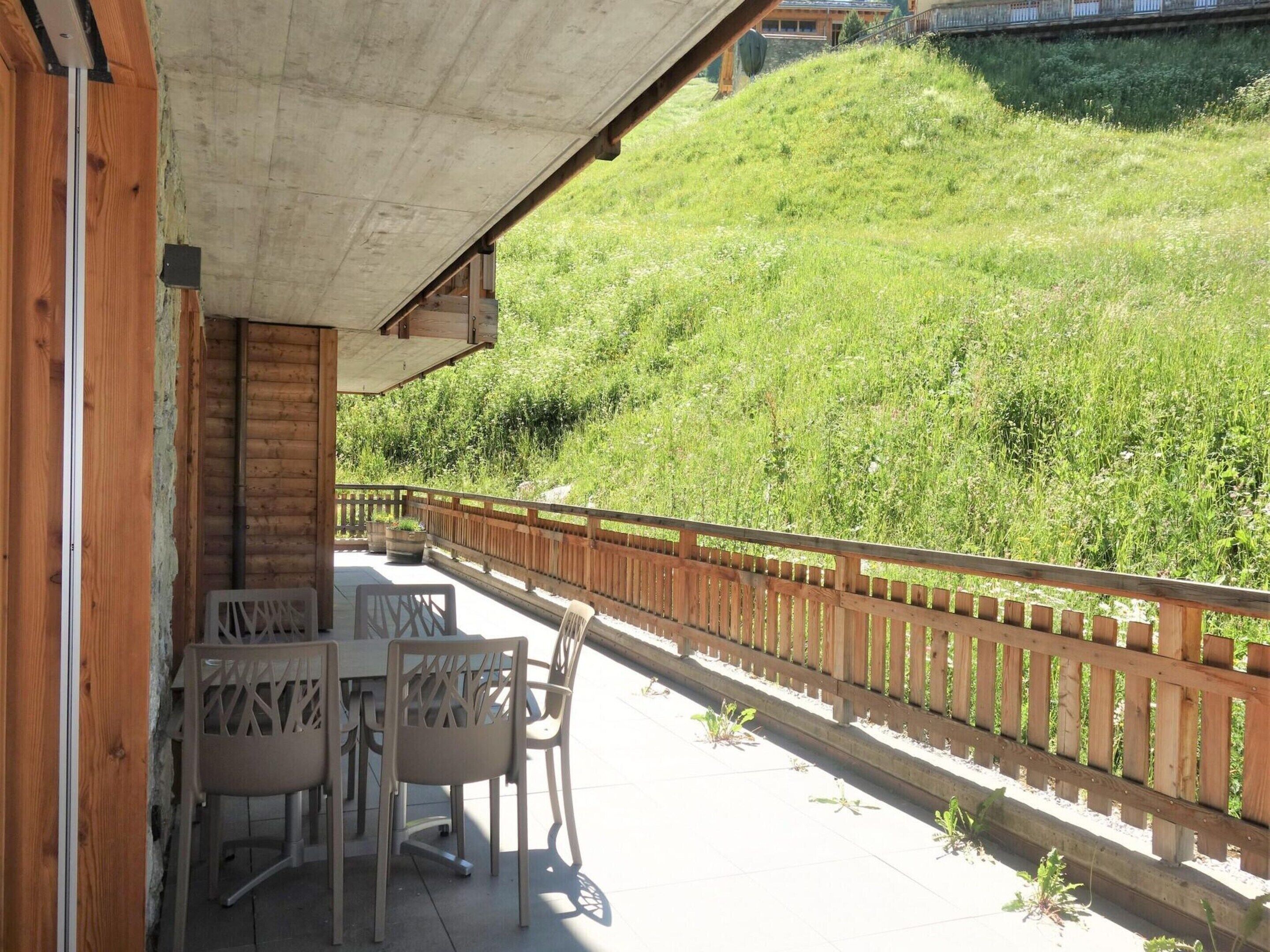 Une terrasse en bois avec une table et des chaises, donnant sur une colline verdoyante.