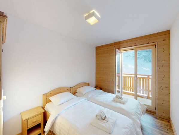 A bedroom with two beds, wooden walls, a small bedside table, and a large window with a view of the outdoors. - Apartment With Swimming Pool Access (Veysonnaz)
