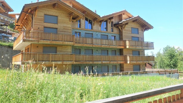 A multi-story wooden chalet with balconies, set in a grassy area. - Apartment With Swimming Pool Access (Veysonnaz)