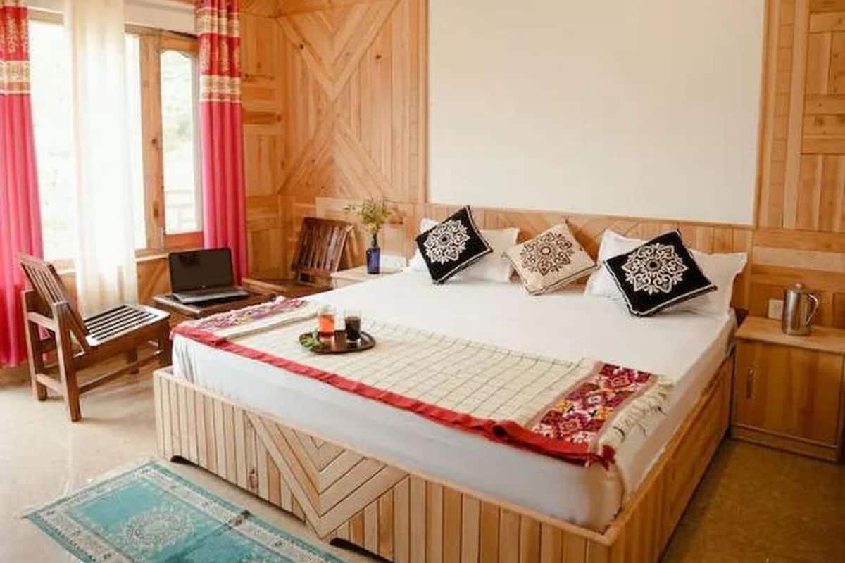 A wooden-paneled bedroom with a bed, a laptop on a chair, and a window with curtains.