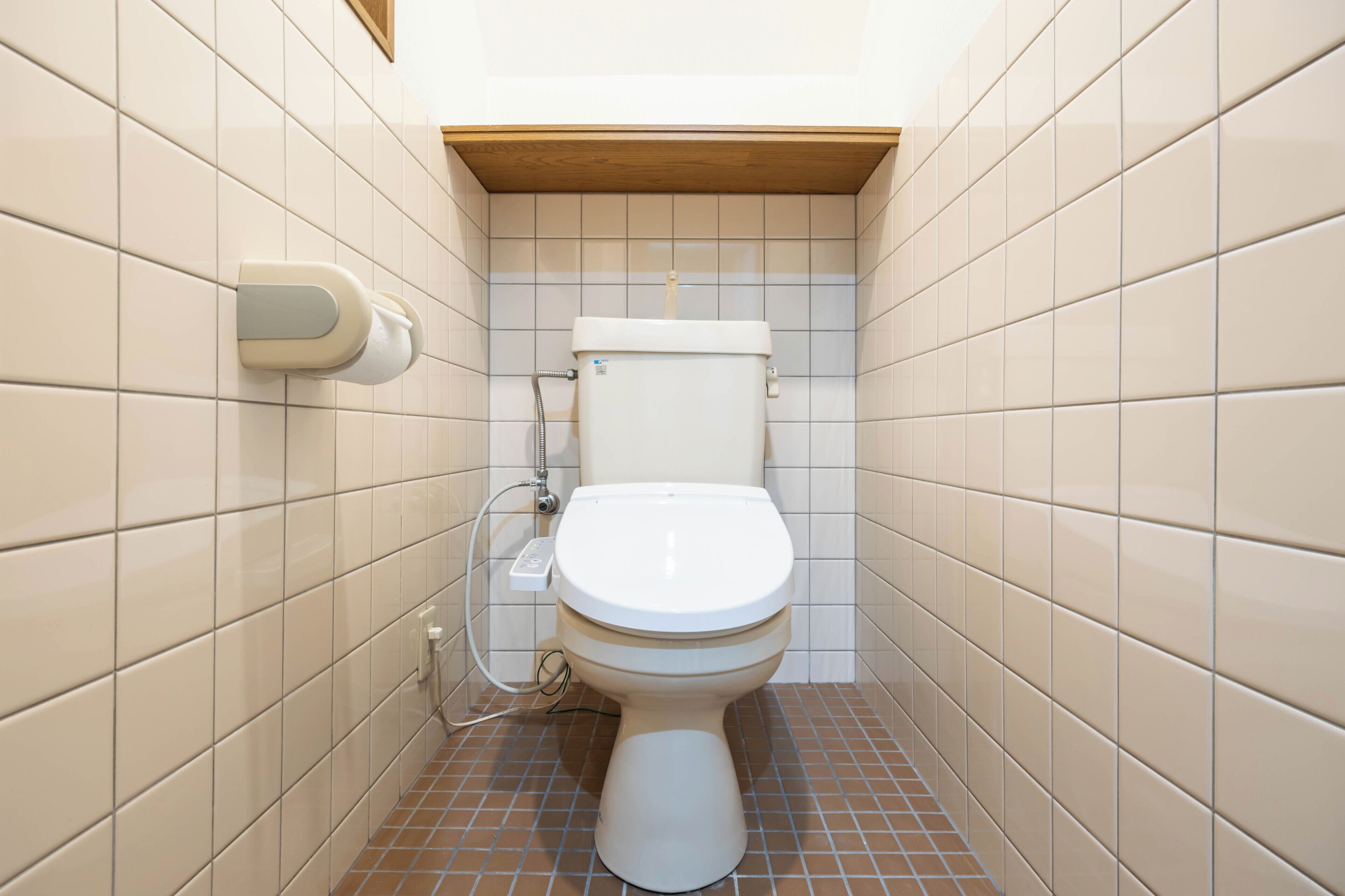Un baño pequeño con azulejos, un inodoro, un dispensador de toallas de papel y un enchufe visible.