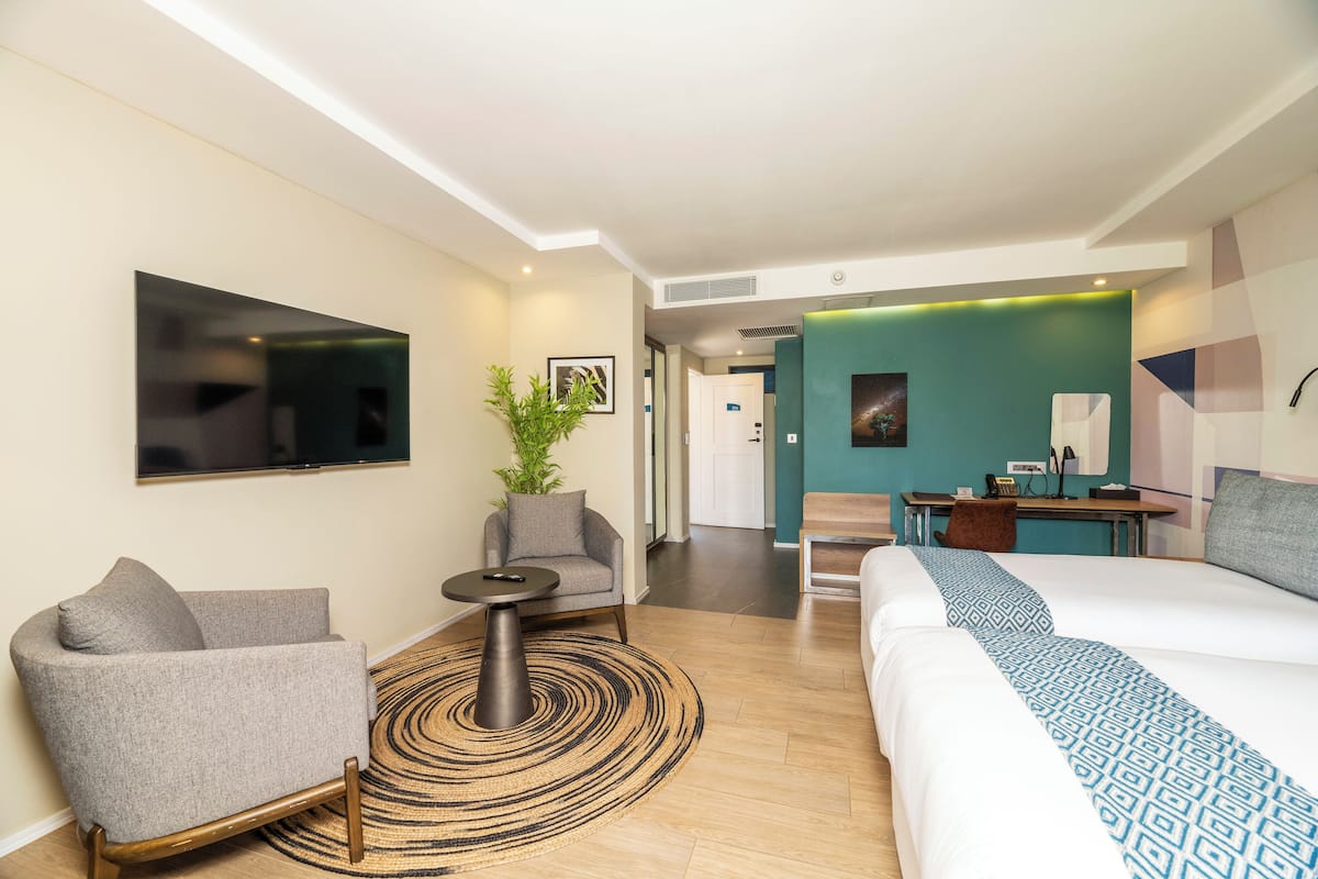 A hotel room with a bed, a sofa, a small table, a TV, and a desk with a chair.