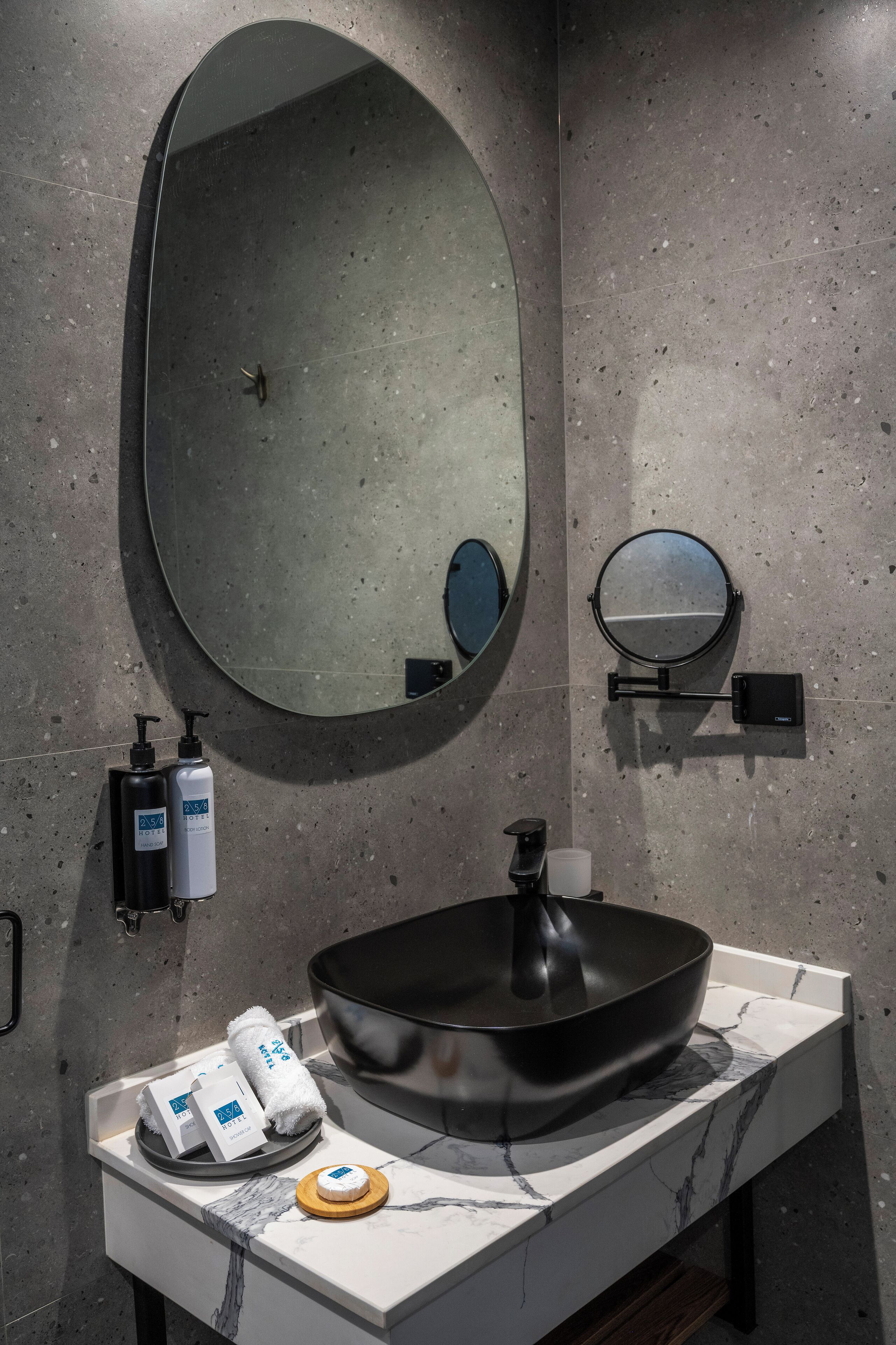 A modern bathroom with a large oval mirror, a round mirror, a black sink, and toiletries on the counter.