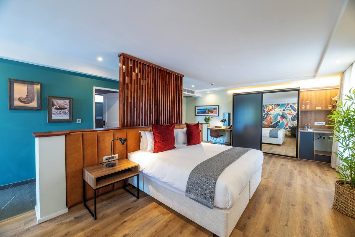 A modern hotel room with a large bed, wooden headboard, bedside table, and a small desk.