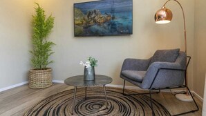 A room with a large painting of a coastal scene, a modern chair, a floor lamp, a round coffee table, and a potted plant. - 258 Hotel (Harare)