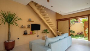 Ein modernes Wohnzimmer mit einem hellblauen Sofa, einer großen Topfpflanze, einem Flachbildfernseher und einer Holztreppe, die in einen Außenbereich führt.