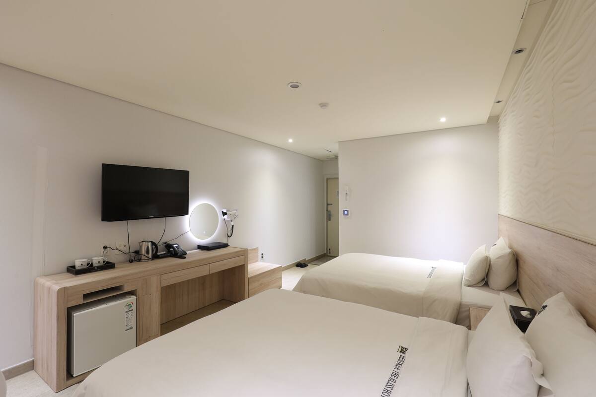 A hotel room with two beds, a TV, a minibar, and a small desk with a mirror.