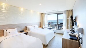 Een hotelkamer met twee bedden, een bureau met telefoon en uitzicht op zee.