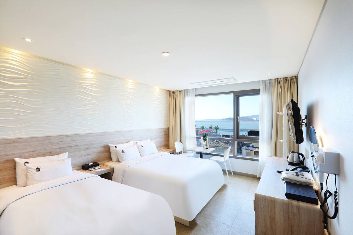 A hotel room with two beds, a desk with a telephone, and a view of the sea.