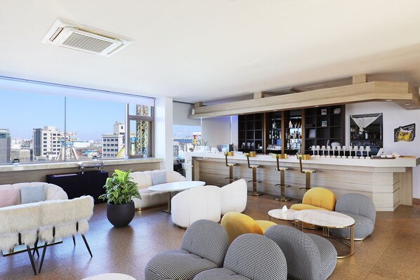 Un salon moderne doté d’un coin bar, de grandes fenêtres et offrant une vue sur la ville.