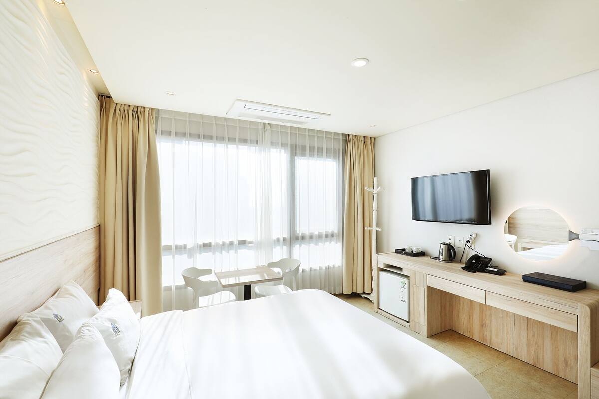 A hotel room with a bed, a desk, a television, and a window with curtains.