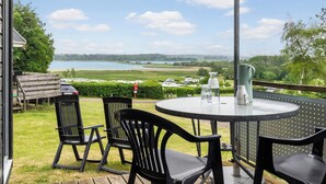 Une terrasse extérieure avec une table ronde et quatre chaises, donnant sur un lac et des champs verdoyants.
