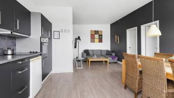 A modern kitchen with dark cabinets, a built-in oven, and a dishwasher. There is a dining area with wicker chairs and a wooden table.