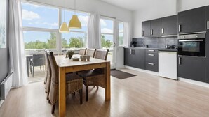 Une cuisine moderne avec des meubles de couleur sombre, un réfrigérateur blanc et une grande fenêtre donnant sur un espace verdoyant.