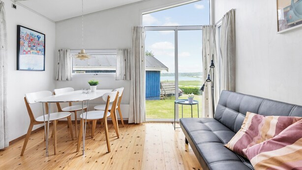 Un salon moderne avec un canapé et une table à manger entourée de chaises. On y trouve une grande fenêtre avec des rideaux, un luminaire au plafond et une petite table sur laquelle est posée une plante.