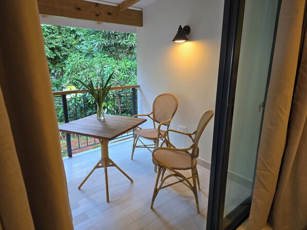 A balcony with a table and two wicker chairs, a potted plant, and a wall-mounted light fixture.