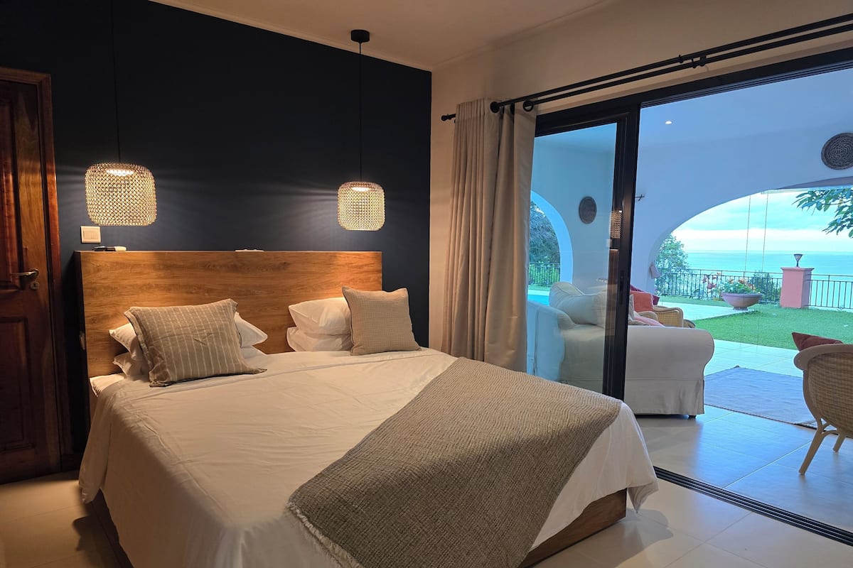 Una camera da letto con un letto grande, due lampade a sospensione e vista sul patio esterno.