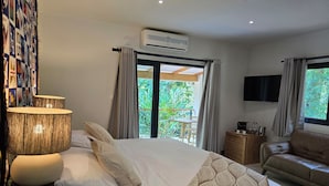 Un dormitorio con una cama grande, un sofá, aire acondicionado, un televisor y un balcón con plantas.